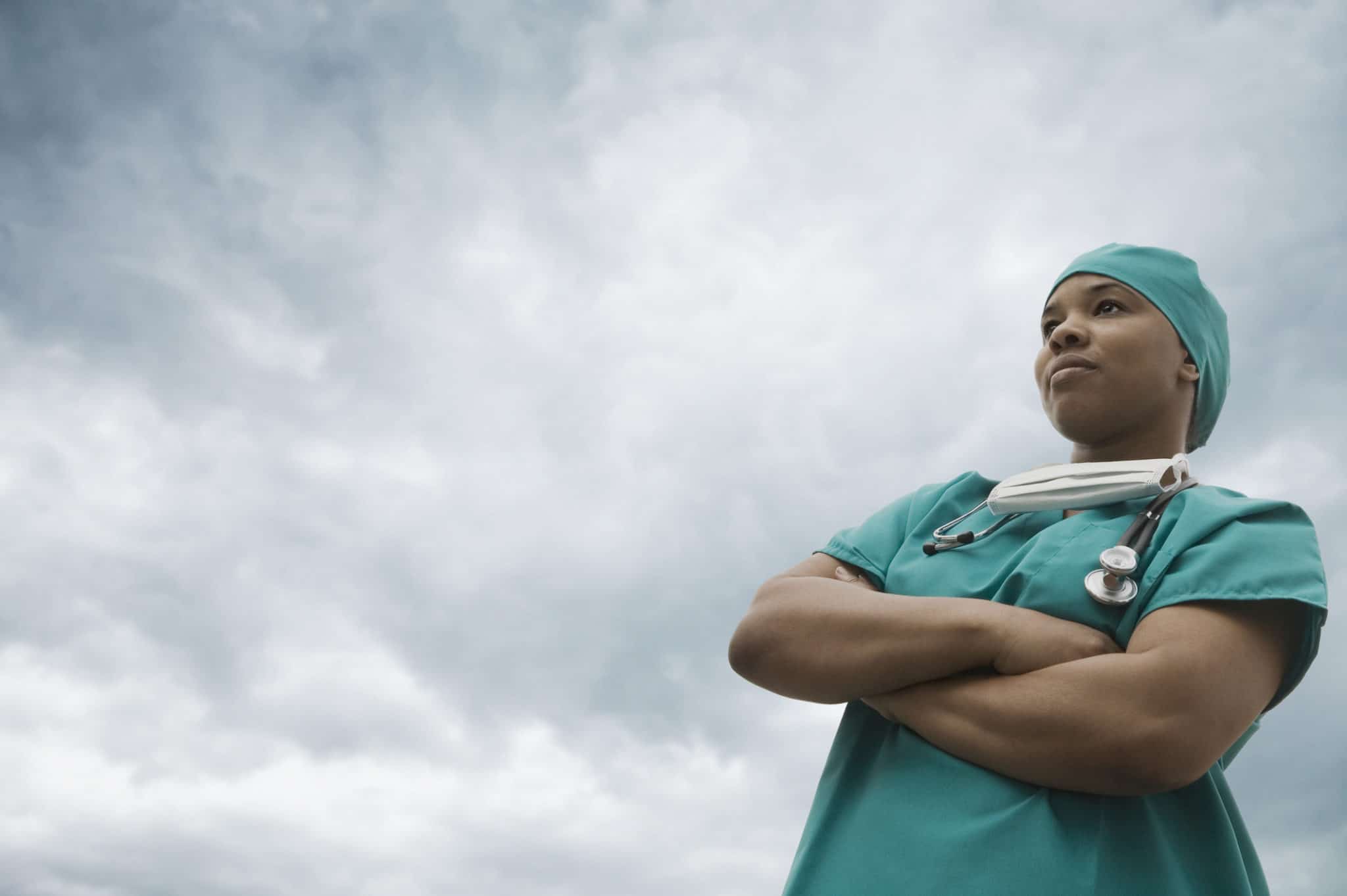 Female surgeon standing in scrubs, with gray sky in background