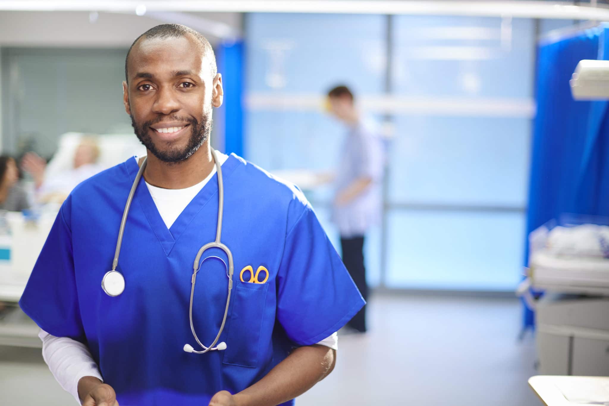 Happy male doctor in blue scrubs smiles at the camera