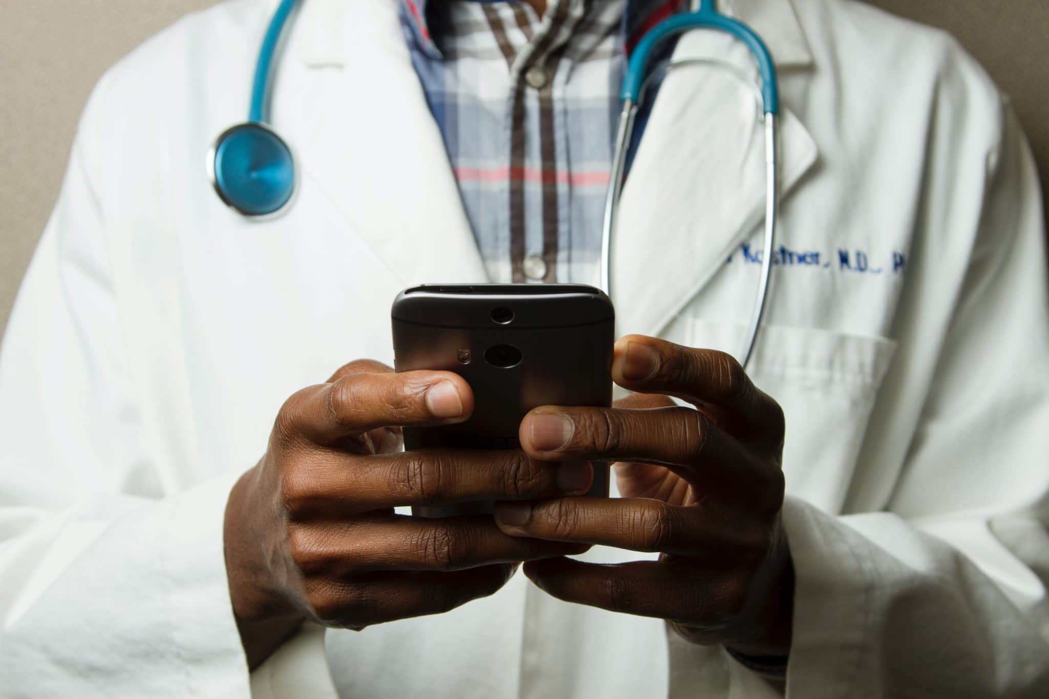 photo of the torso of a person in a white coat with a stethoscope around their neck, holding a cell phone
