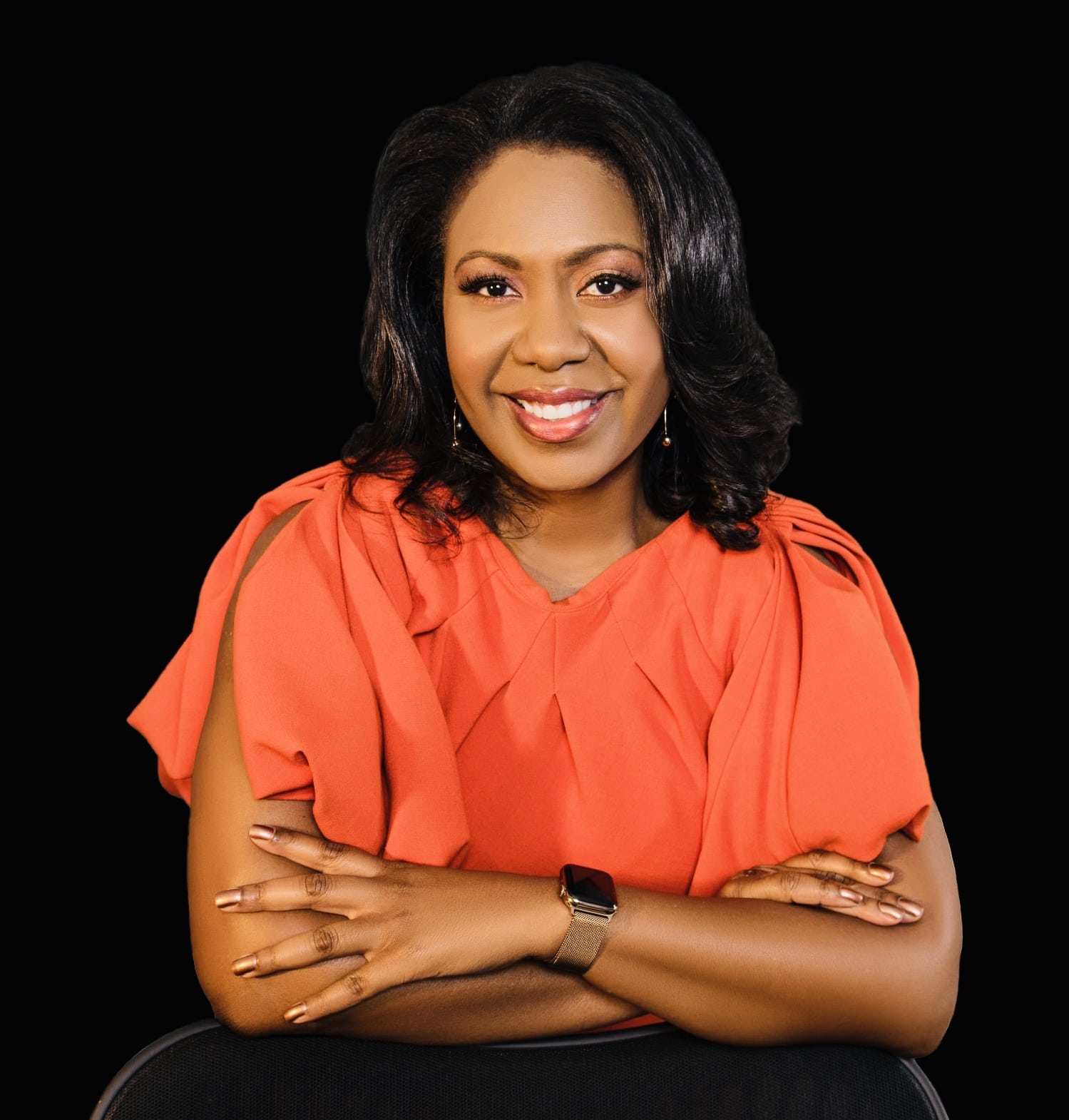 Photo of NMF President and CEO Michellene Davis in front of a black background wearing an orange blouse.