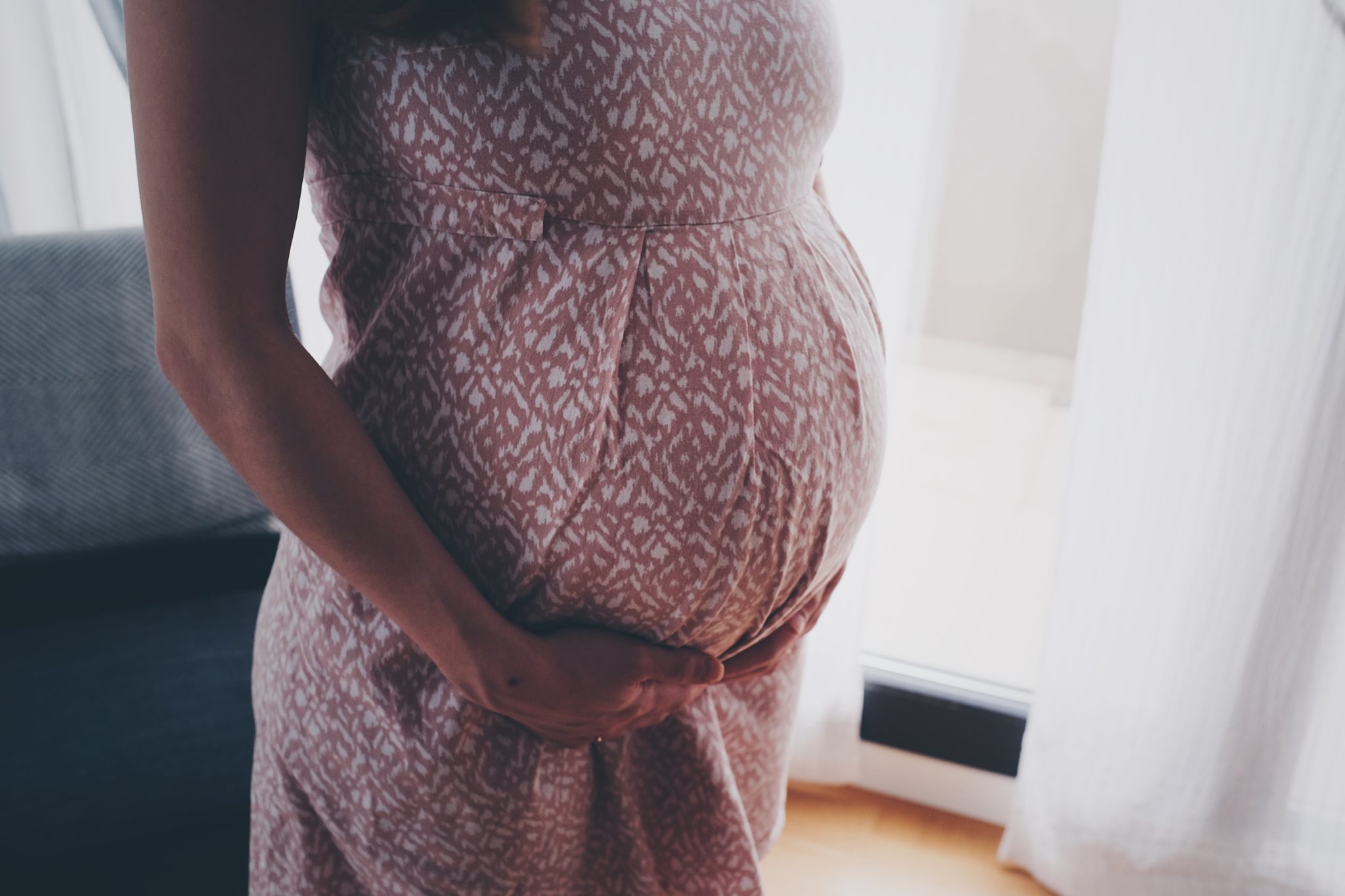 photo of a pregnant woman's torso, and she is clasping her hands below her belly