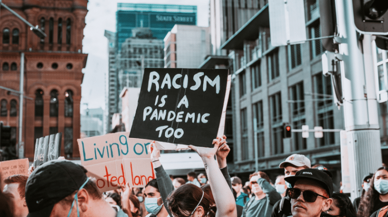 Picture of protestors with a sign that says "racism is a pandemic too"