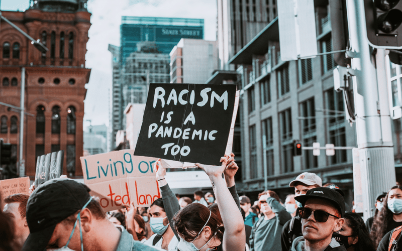 Picture of protestors with a sign that says "racism is a pandemic too"
