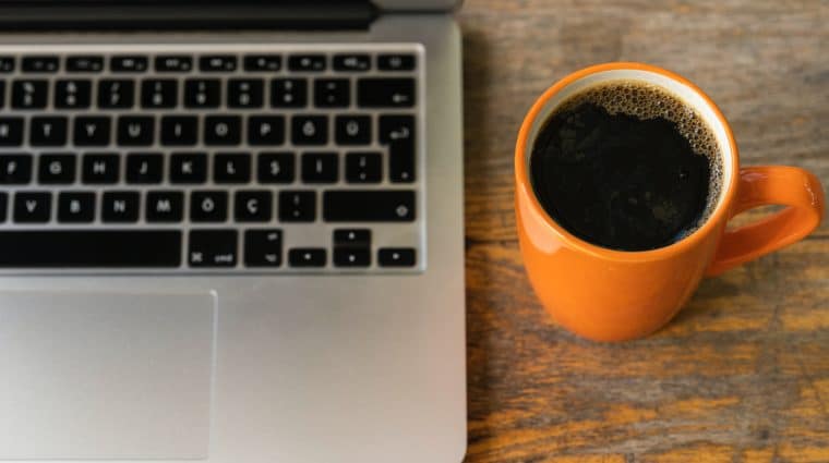 Photo of an open laptop and an orange mug with black coffee