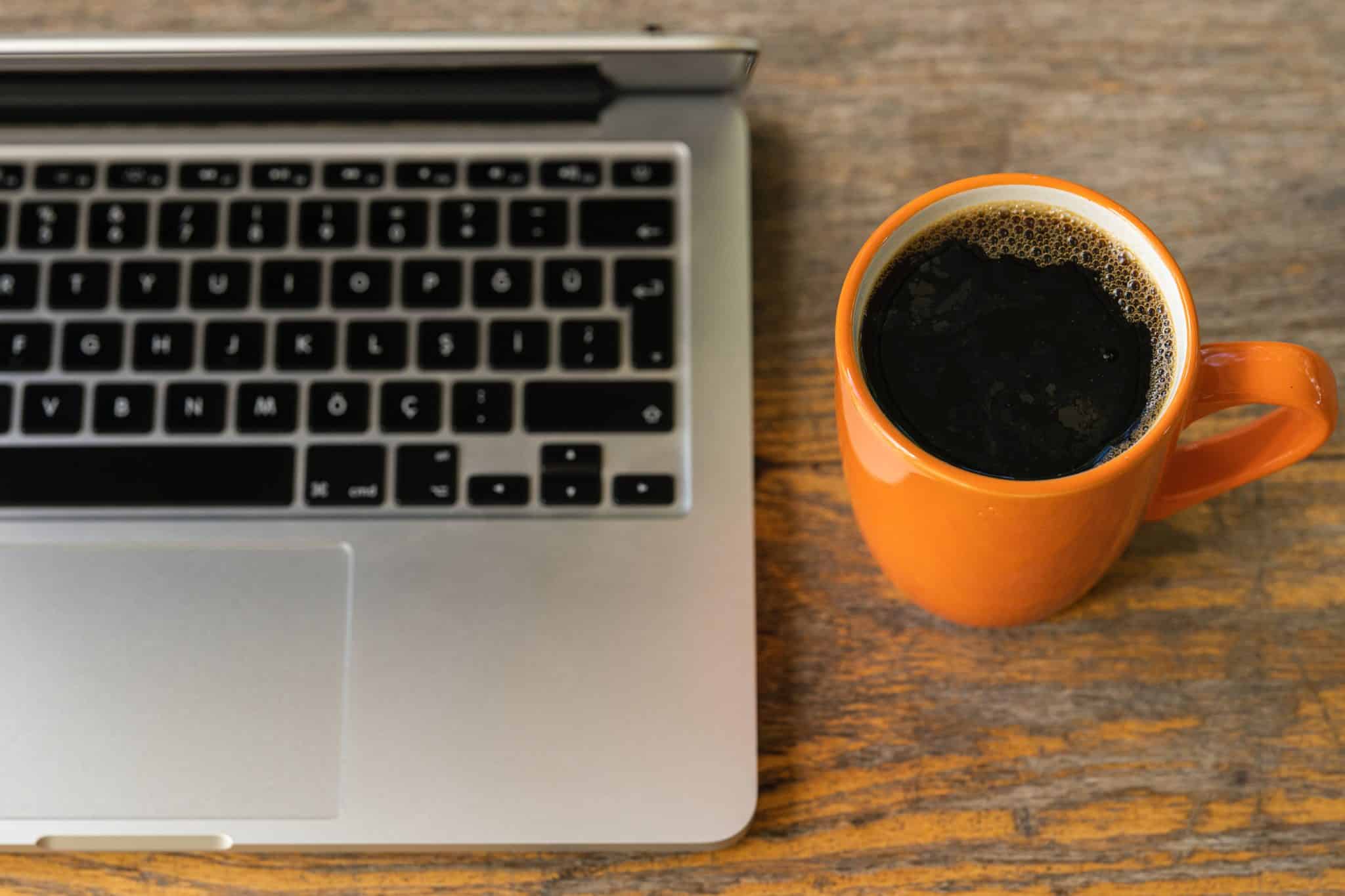 Photo of an open laptop and an orange mug with black coffee