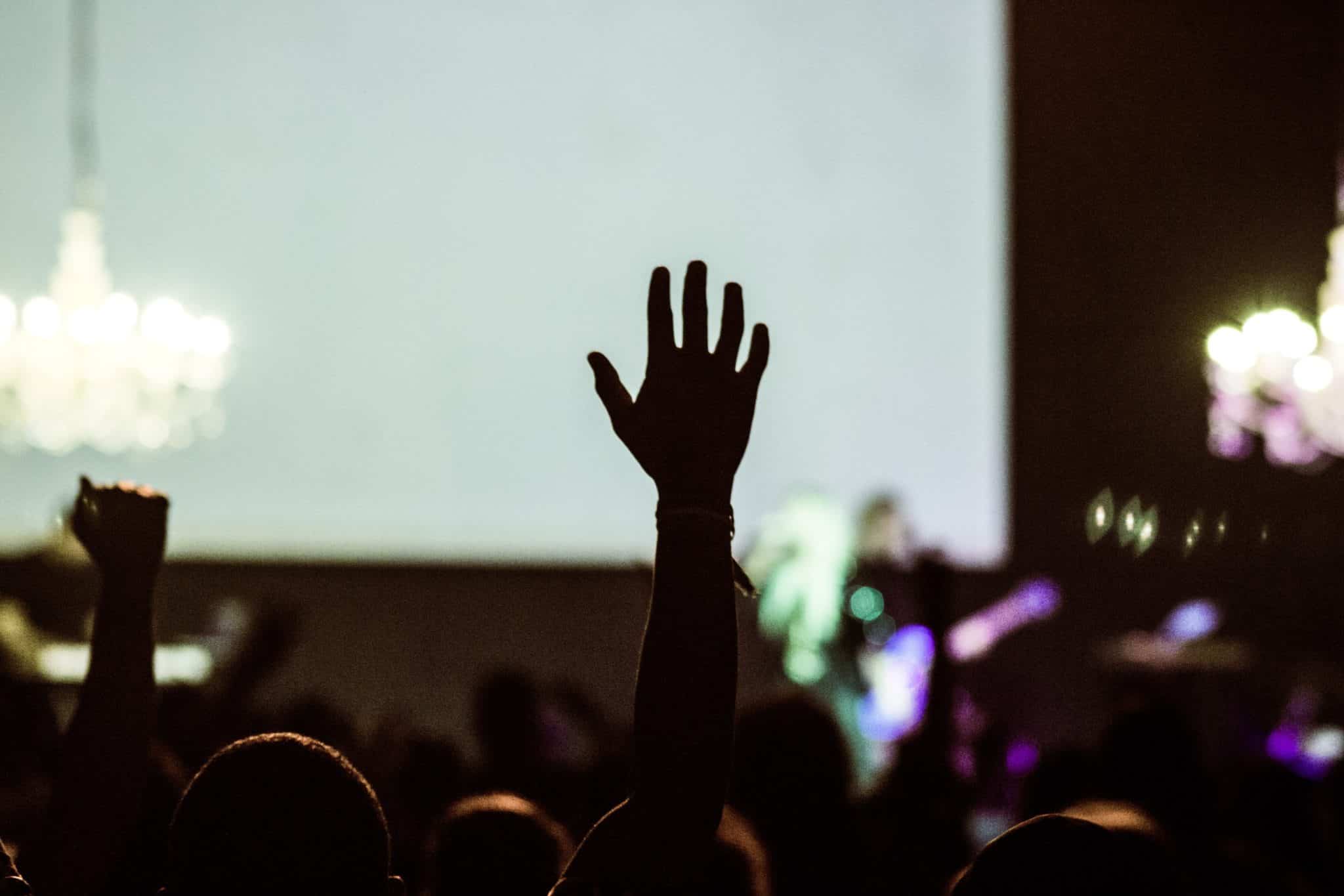 Photo of a crowd in front of a stage with one person's hand raised in silhouette