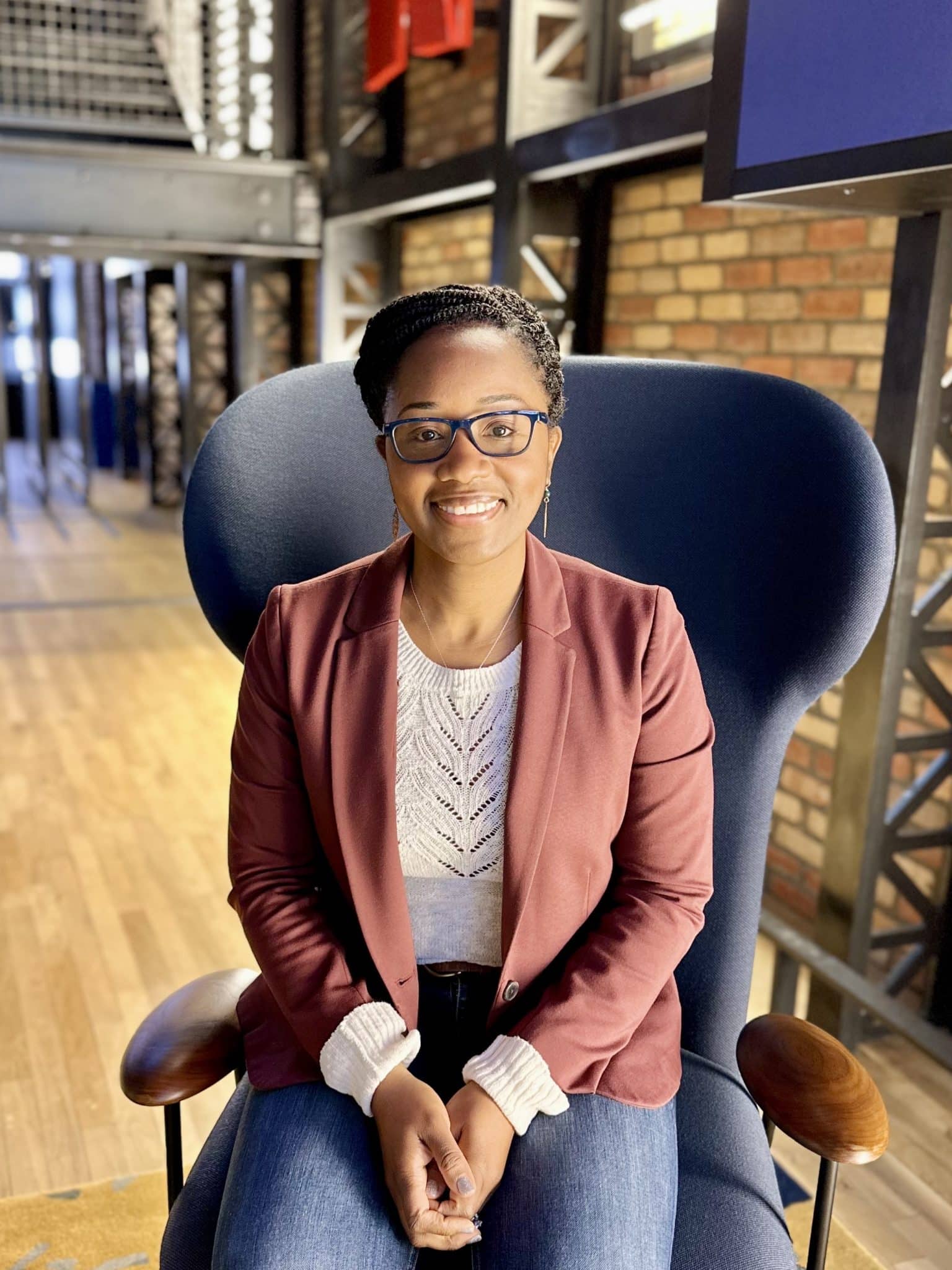 Photo of Dr. Tonya Walker seated in a high backed chair, wearing a redish blazer, glasses, white blouse, and smiling into the camera.