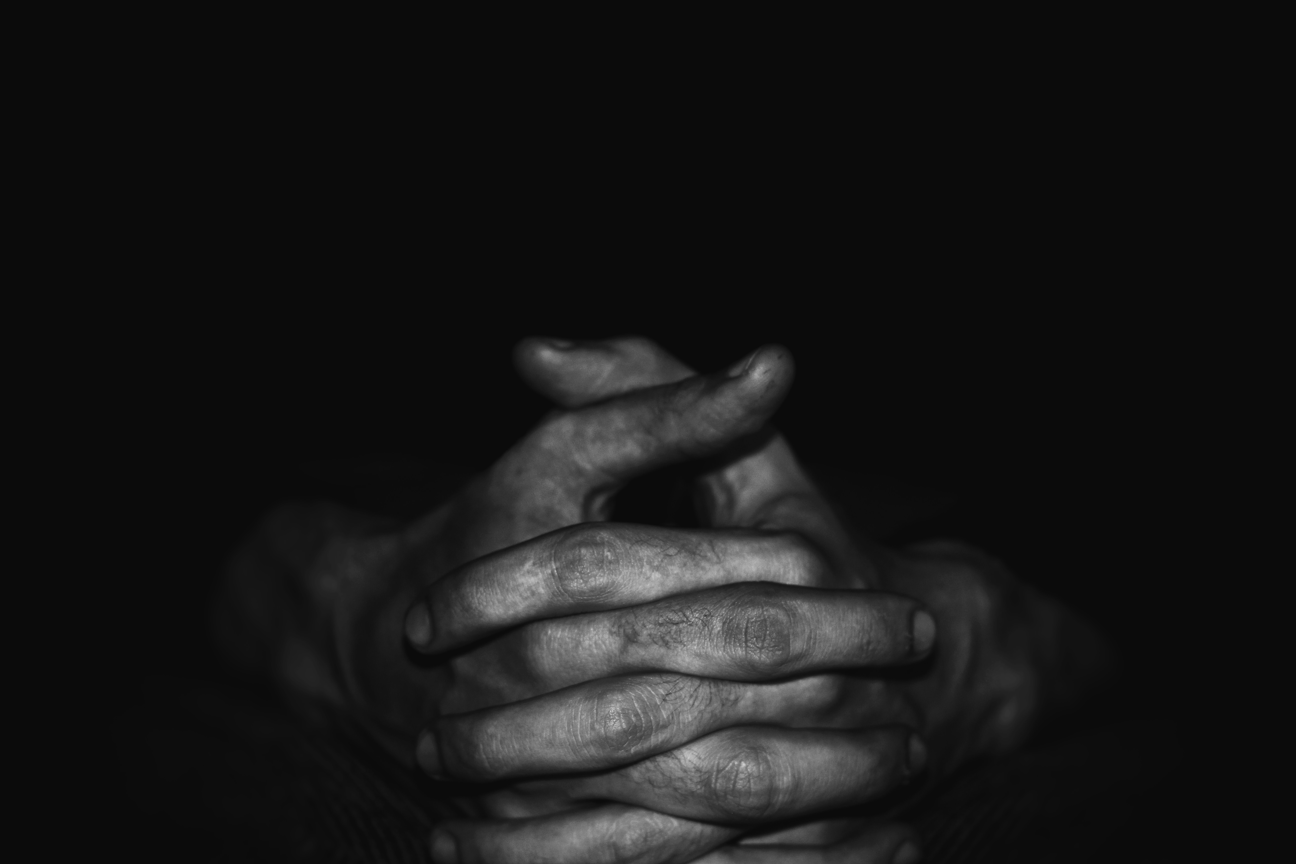 A photo with a black background with a person clasping their hands.