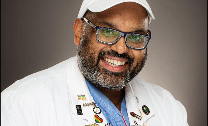 Photo of Dr. Jerry Abraham wearing a white coat and hat, and a blue shirt. He is wearing glasses and smiling into the camera.