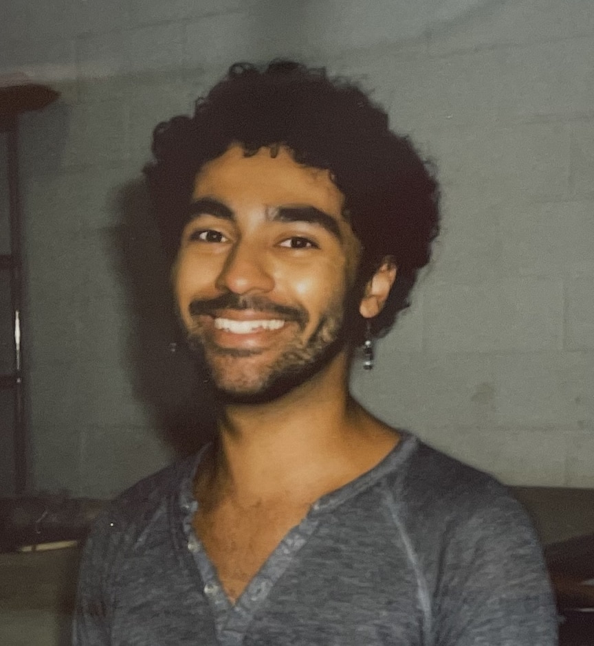 Photo of artist Miguel Lastra smiling into the camera. He is wearing a gray shirt