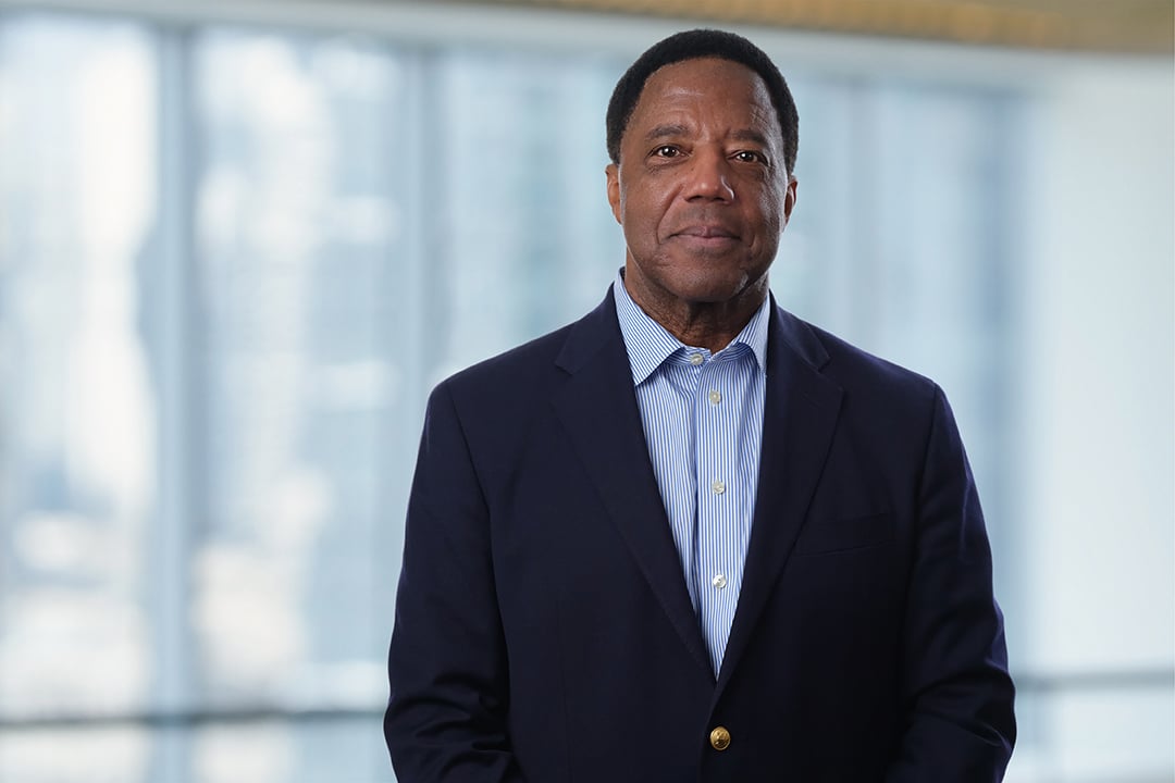 Lloyd H Dean Photo of Lloyd Dean wearing a black jacket and blue shirt, standing in front of a large window