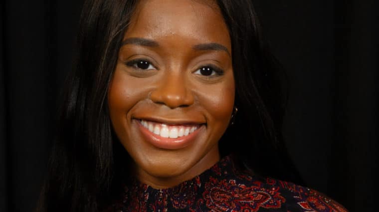 Photo of Dr. Prisca Osuji smiling at the camera wearing a brown and black top.