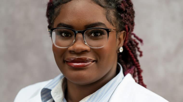 Photo of Faneese Muyah. She is wearing glasses, has her hair pulled back, and is wearing a white doctor's coat.