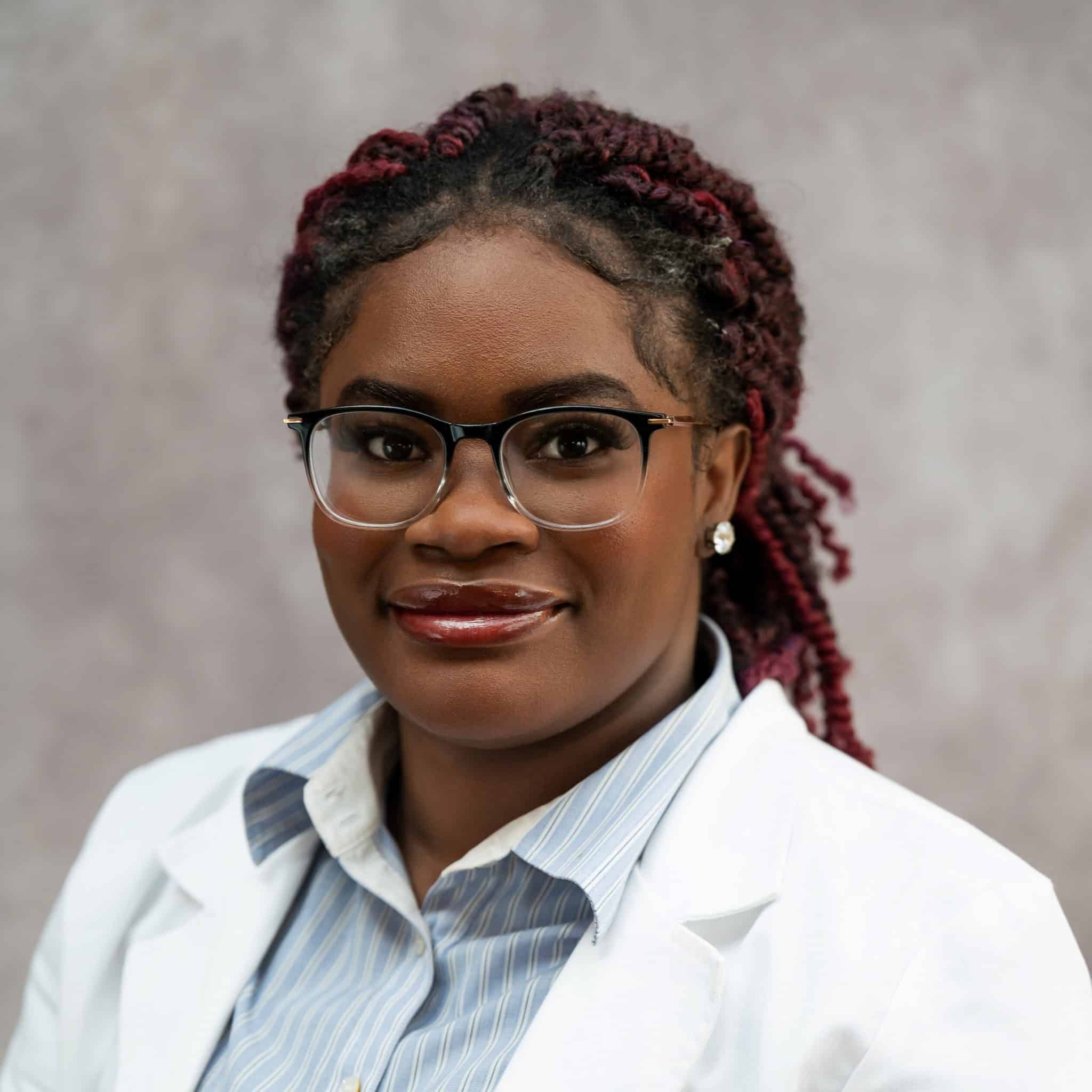 Photo of Faneese Muyah. She is wearing glasses, has her hair pulled back, and is wearing a white doctor's coat.