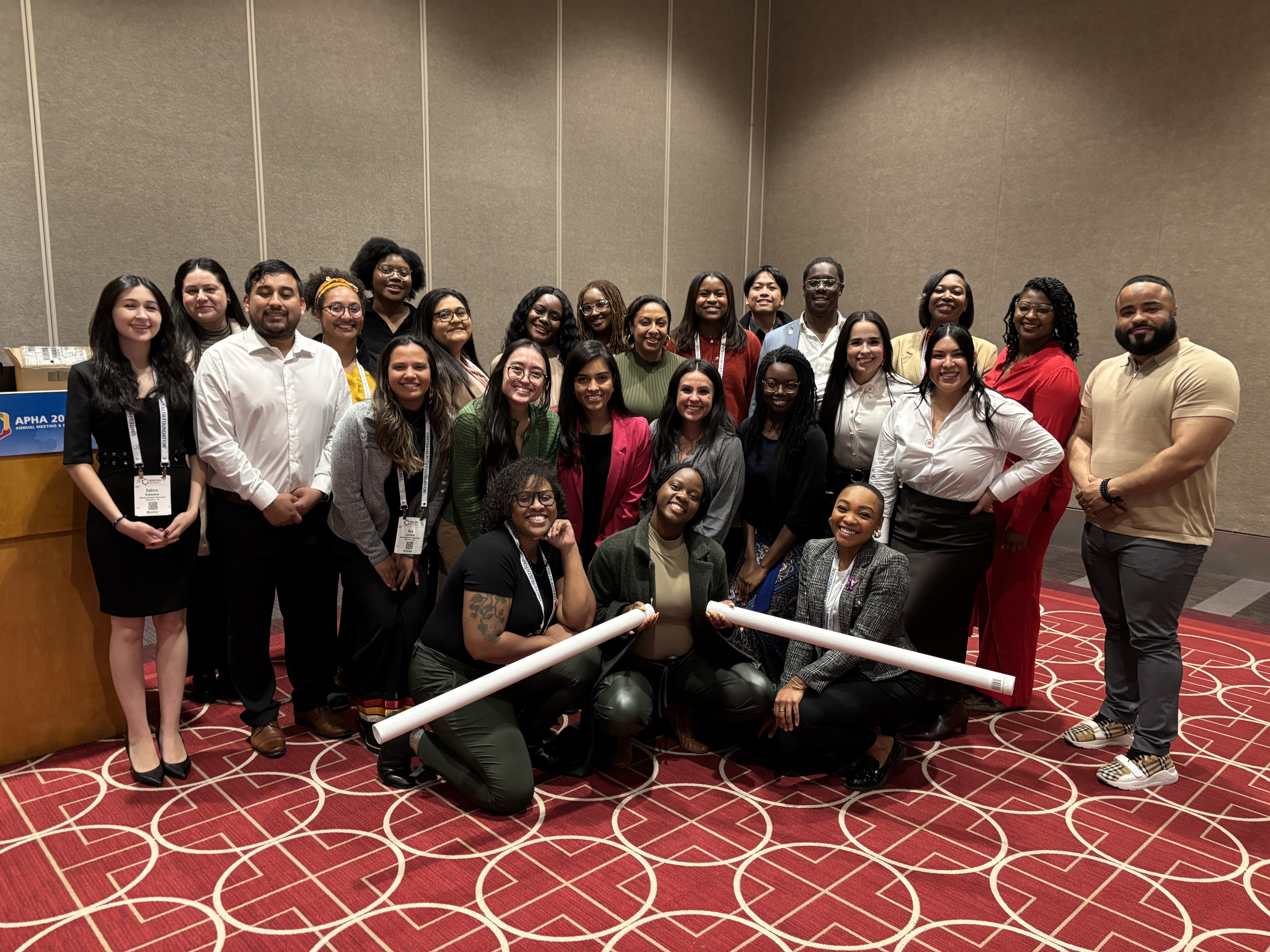 A group of scholars standing and kneeling posing for a photo on a red carpet