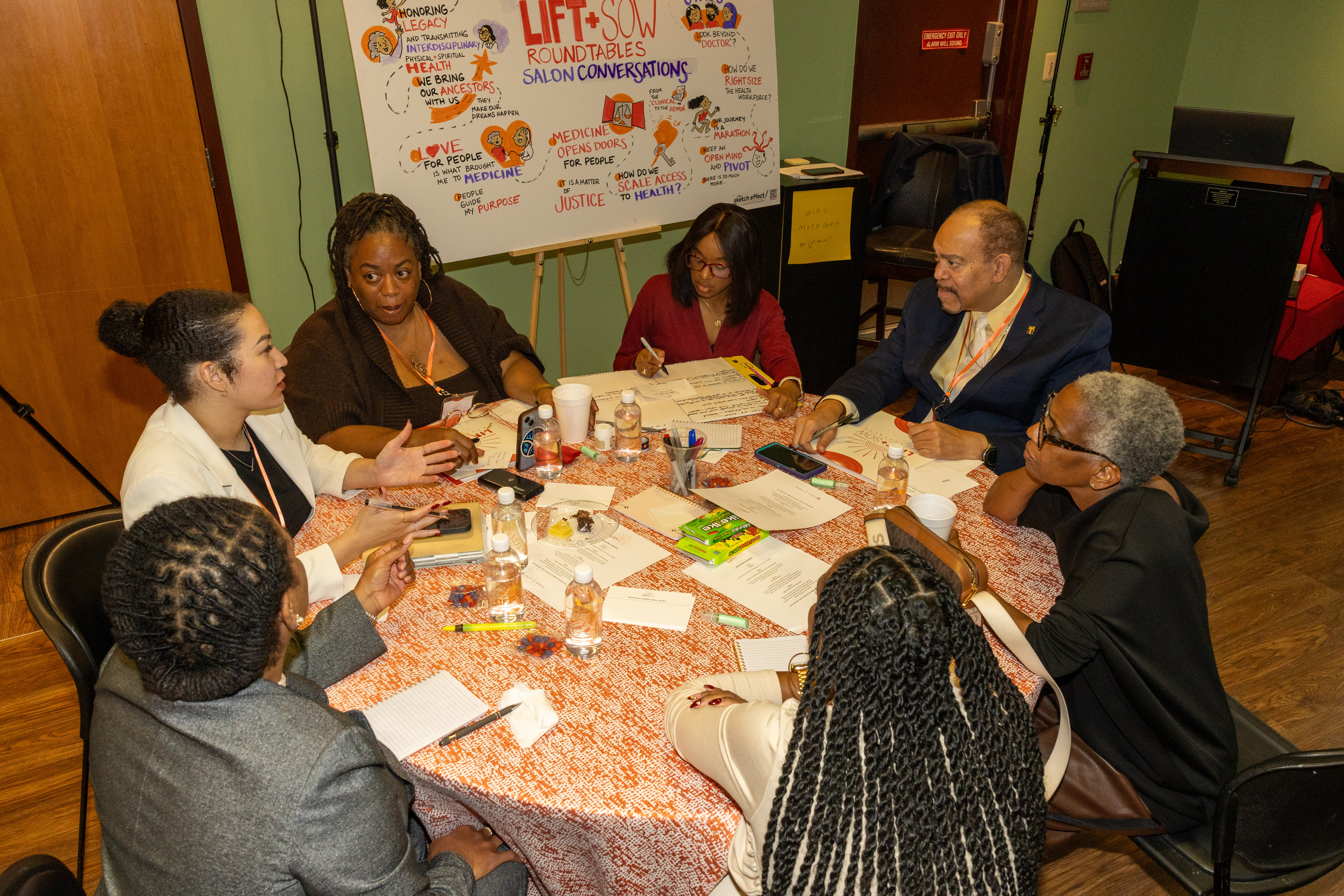 Photo of seven roundtable participants, seated around a round table, conversing.