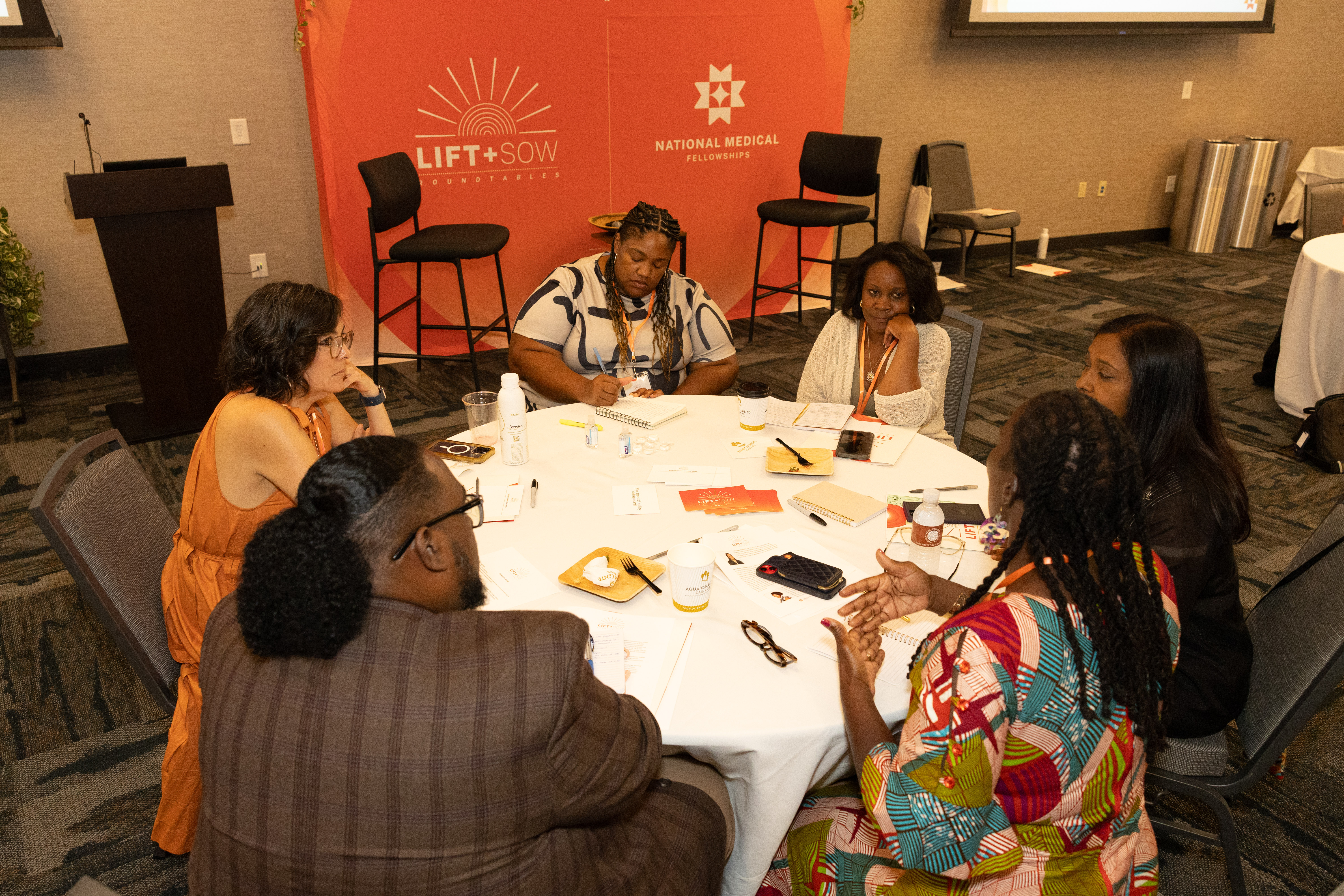 Six people are seated around a round table in deep discussion