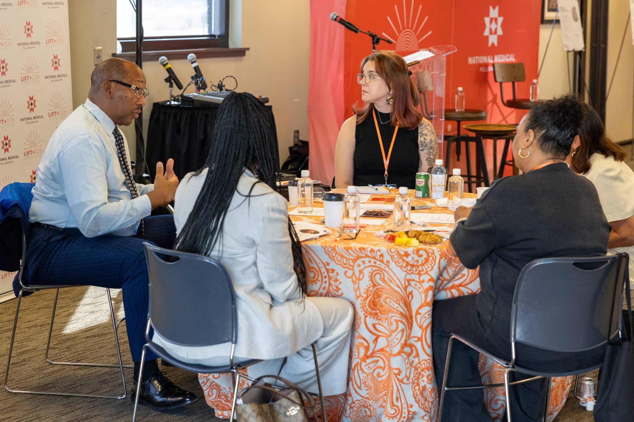 Roundtable participants are seated at a round table and listening to a man at the table speak and gesture.