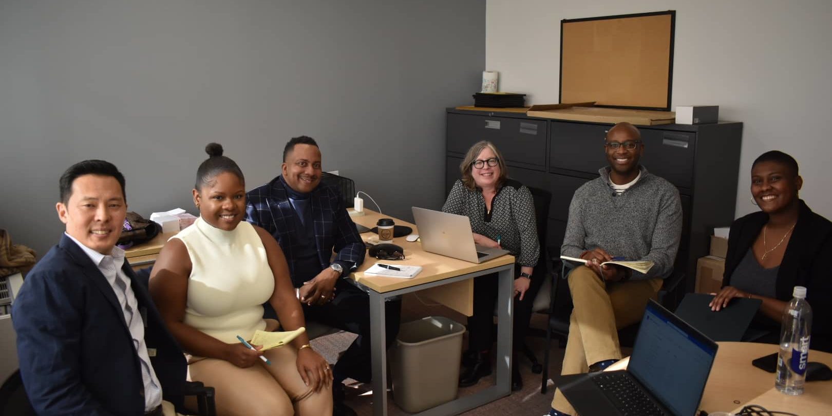 Six individuals sitting around a desk in an office.