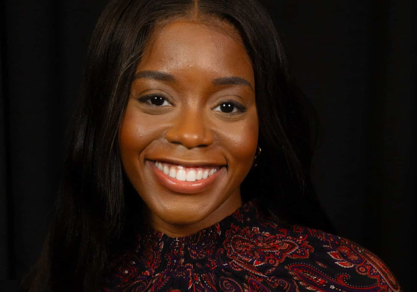 Photo of Dr. Prisca Osuji smiling at the camera wearing a brown and black top.
