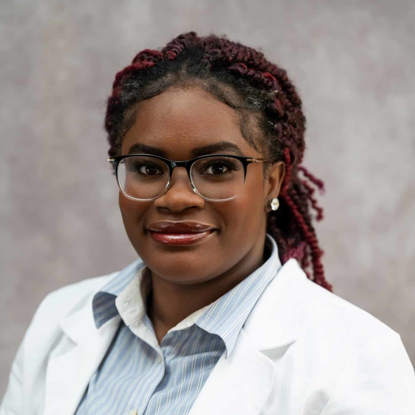 Photo of Faneese Muyah. She is wearing glasses, has her hair pulled back, and is wearing a white doctor's coat.