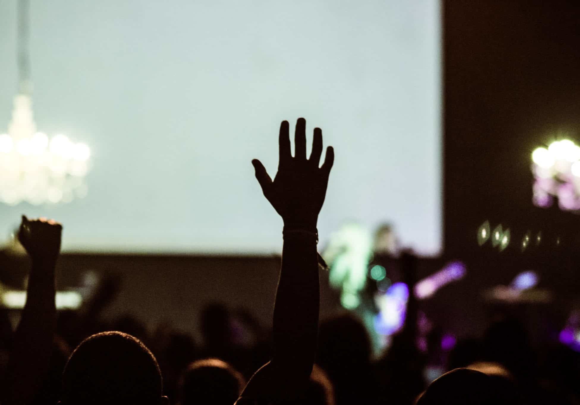 Photo of a crowd in front of a stage with one person's hand raised in silhouette