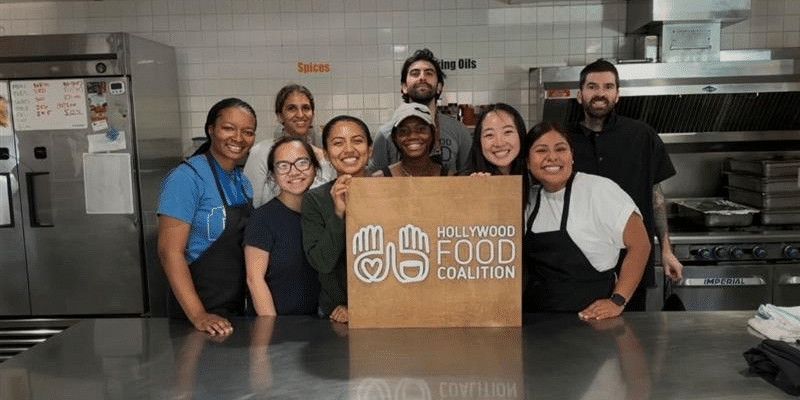 Photo of a group of young people in a commercial kitchen smiling behind a sign reading Hollywood Food Coalition