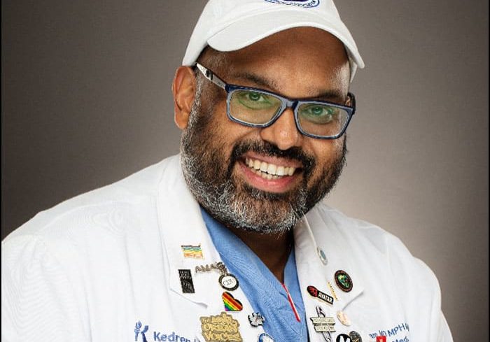 Photo of Dr. Jerry Abraham wearing a white coat and hat, and a blue shirt. He is wearing glasses and smiling into the camera.